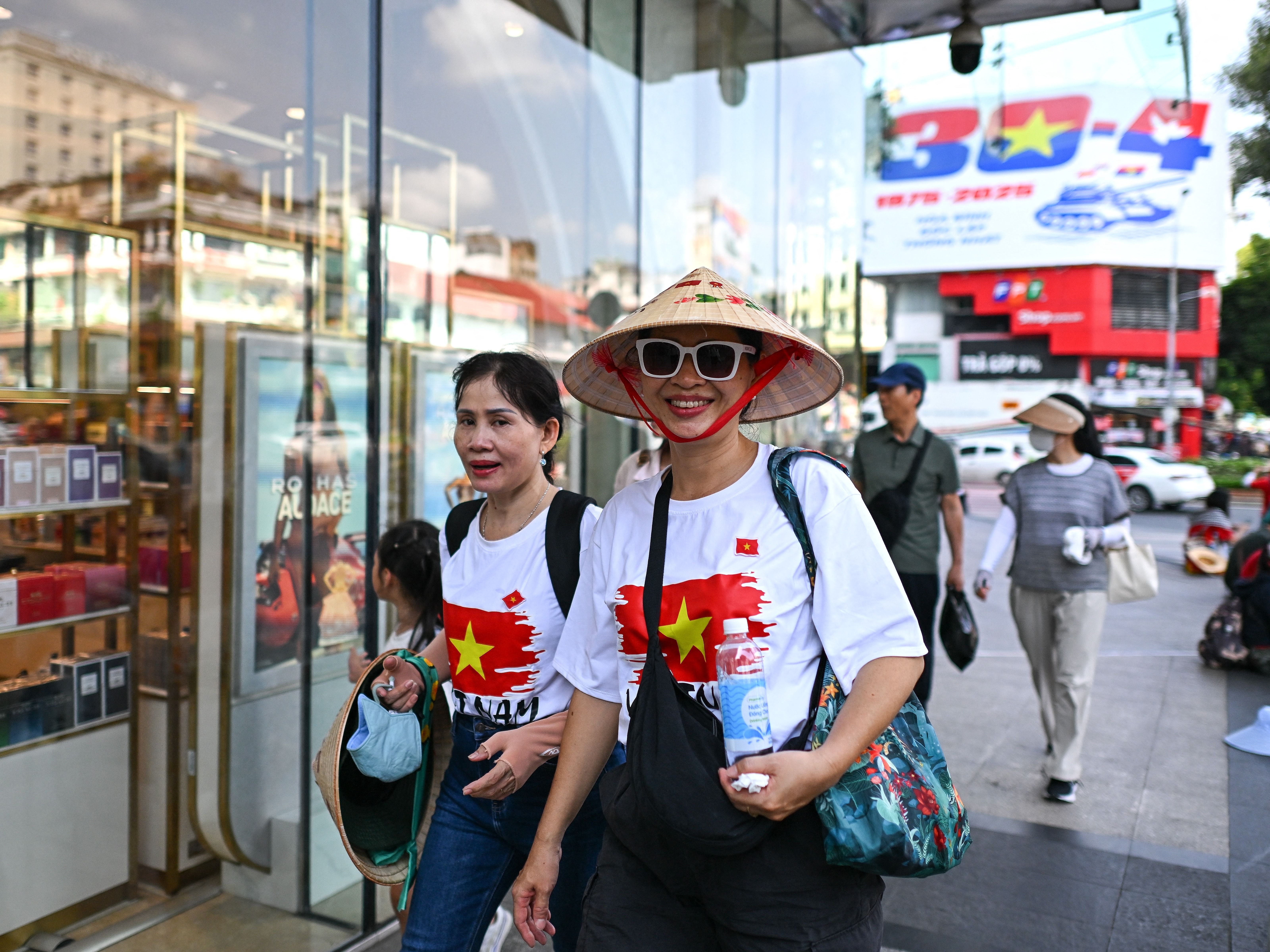caption: Women wearing Vietnamese national flag T-shirts walk past the Saigon Centre shopping complex in Ho Chi Minh City on April 29, 2025, ahead of celebrations to mark the 50th anniversary of the end of the Vietnam War.