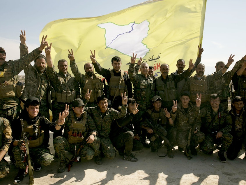 caption: U.S.-backed Syrian Democratic Forces (SDF) fighters pose for a photo in Baghouz, Syria, in March after the SDF declared the area free of Islamic State militants.