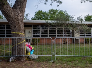caption: Balloons are seen wrapped around a tree in caution tape at Robb Elementary School on May 31, 2022 in Uvalde, Texas, a week after the school shooting.