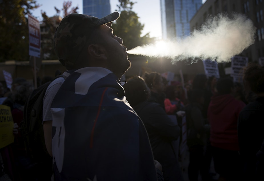 caption: Armen, a member of the UW College Republicans blows smoke into the air during the 'Cancel Kavanaugh - We Believe Survivors' march and rally on Thursday, October 4, 2018, at Westlake Park in Seattle.