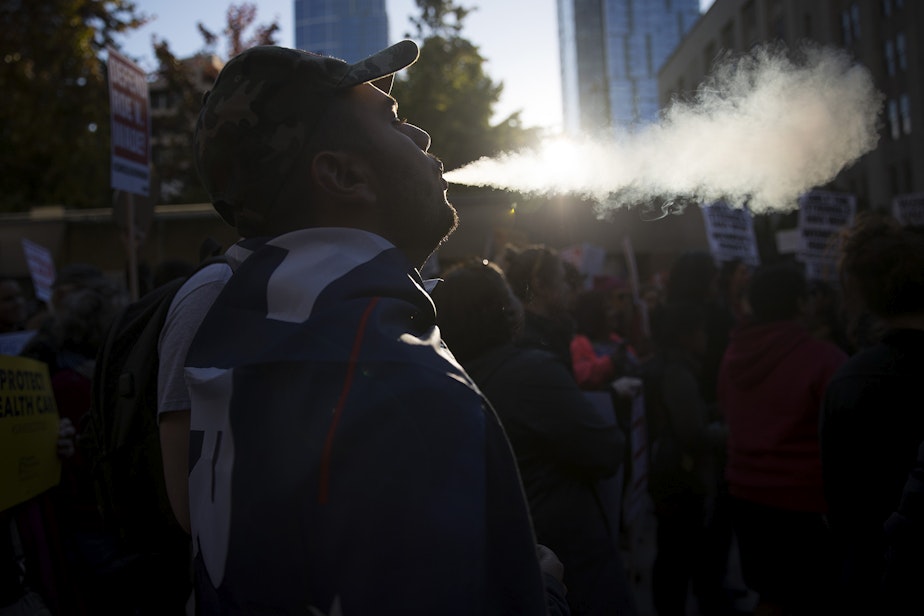 caption: Armen, a member of the UW College Republicans blows smoke into the air during the 'Cancel Kavanaugh - We Believe Survivors' march and rally on Thursday, October 4, 2018, at Westlake Park in Seattle.