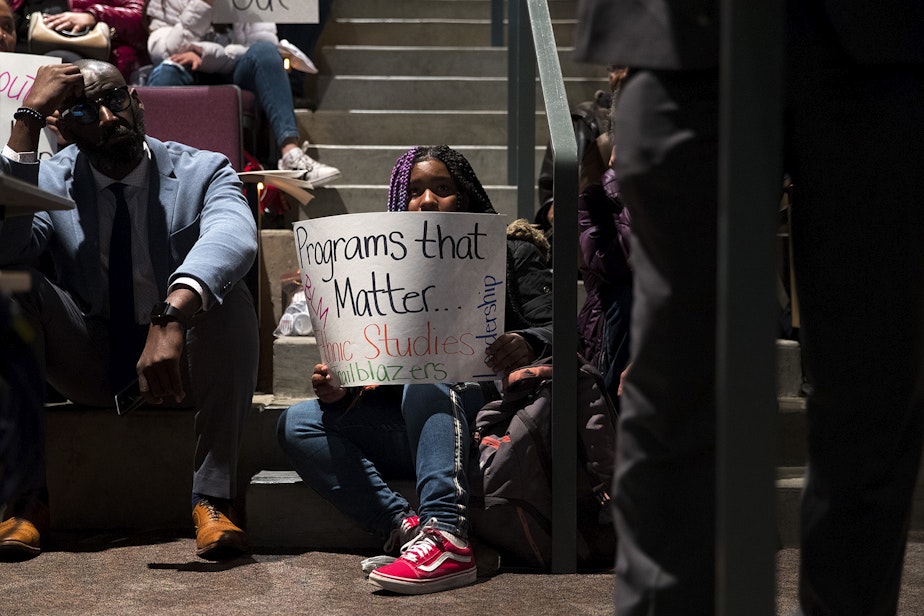 caption: Sharae Miller, a 9th-grade student at Garfield high school holds a sign showing support for ethnic studies programs at a public meeting to address concerns about abusive teachers on Thursday, February 13, 2020, at the Quincy Jones Performing Arts Center at Garfield High School in Seattle. 