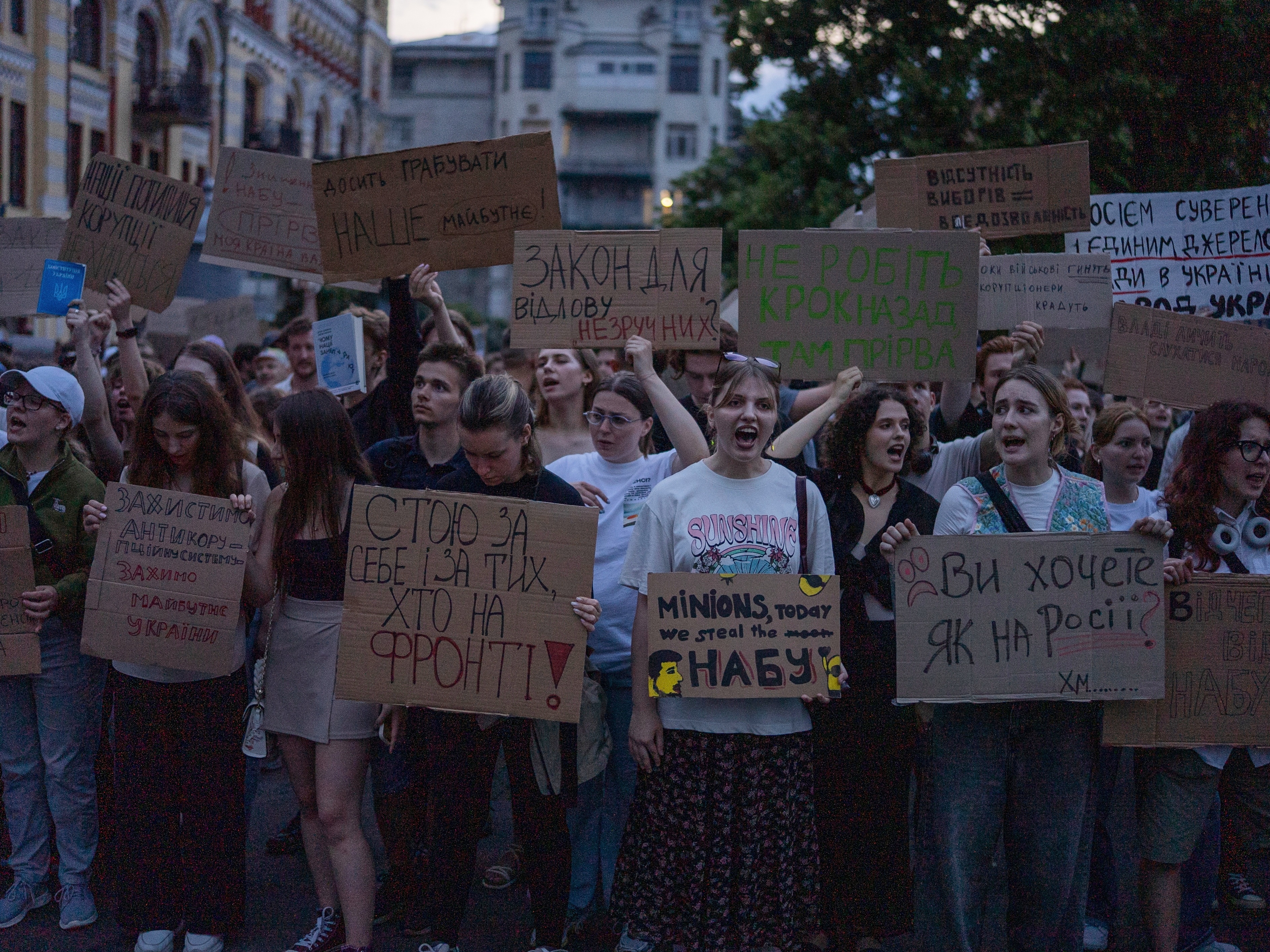caption: Protestant chant while holding banners that read "I stand for you, and for those who are on the frontline", "Do you want it like in Russia", "Stop robbing our future" during a protest against a law targeting anti-corruption institutions in central Kyiv, Ukraine on Tuesday.
