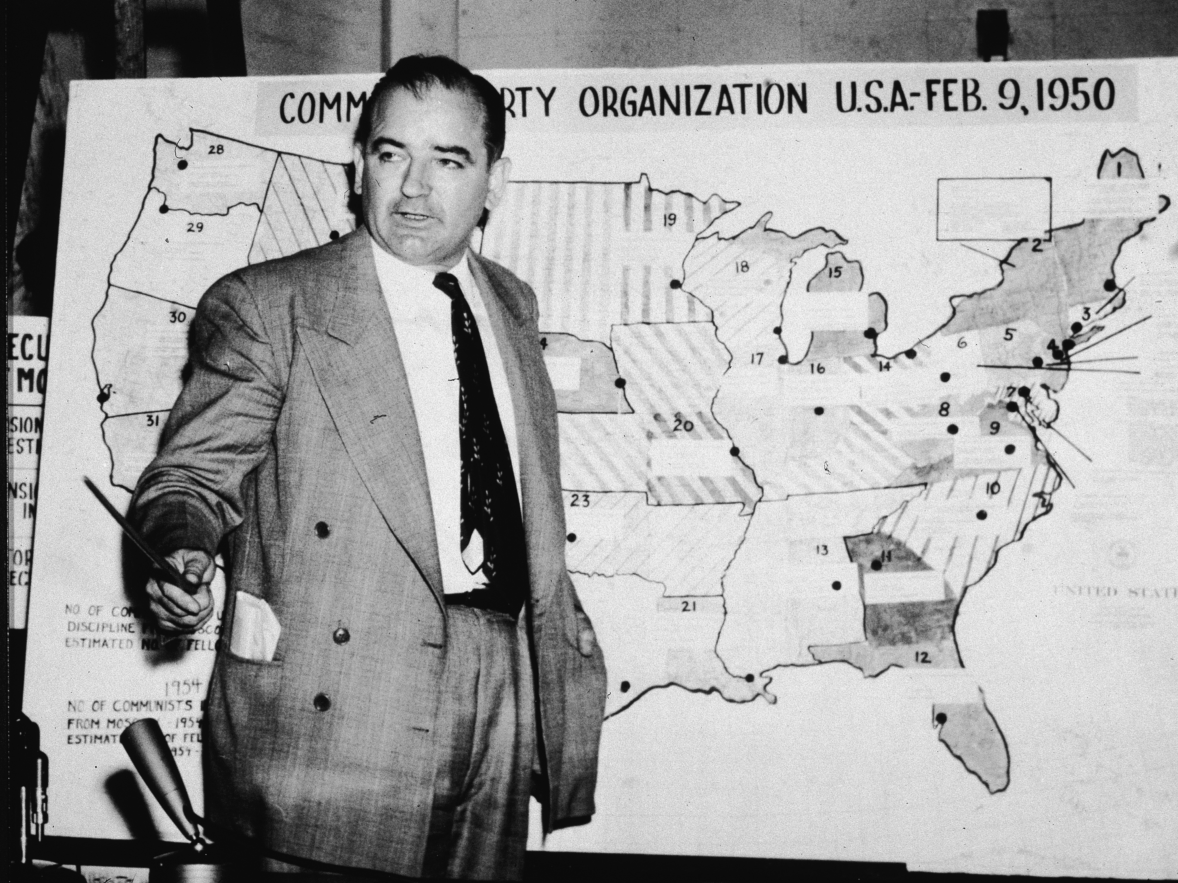 caption: Sen. Joe McCarthy, R-Wis., testifies during hearings in Washington, D.C., on June 9, 1954. McCarthy stands before a map that charts alleged communist activity in the United States.