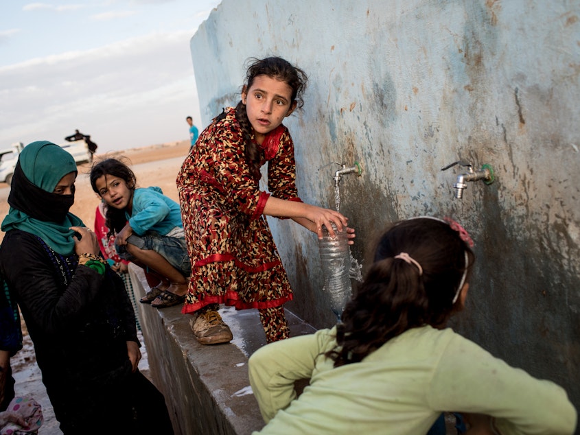 caption: Access to water is increasingly entangled with conflict situations. (Above) A young girl fills a bottle at a pump station at a camp for internally displaced people in Ain Issa, Syria.