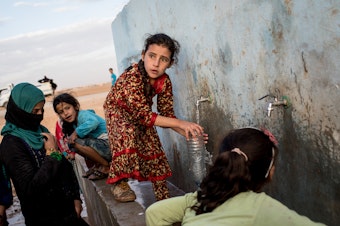 caption: Access to water is increasingly entangled with conflict situations. (Above) A young girl fills a bottle at a pump station at a camp for internally displaced people in Ain Issa, Syria.