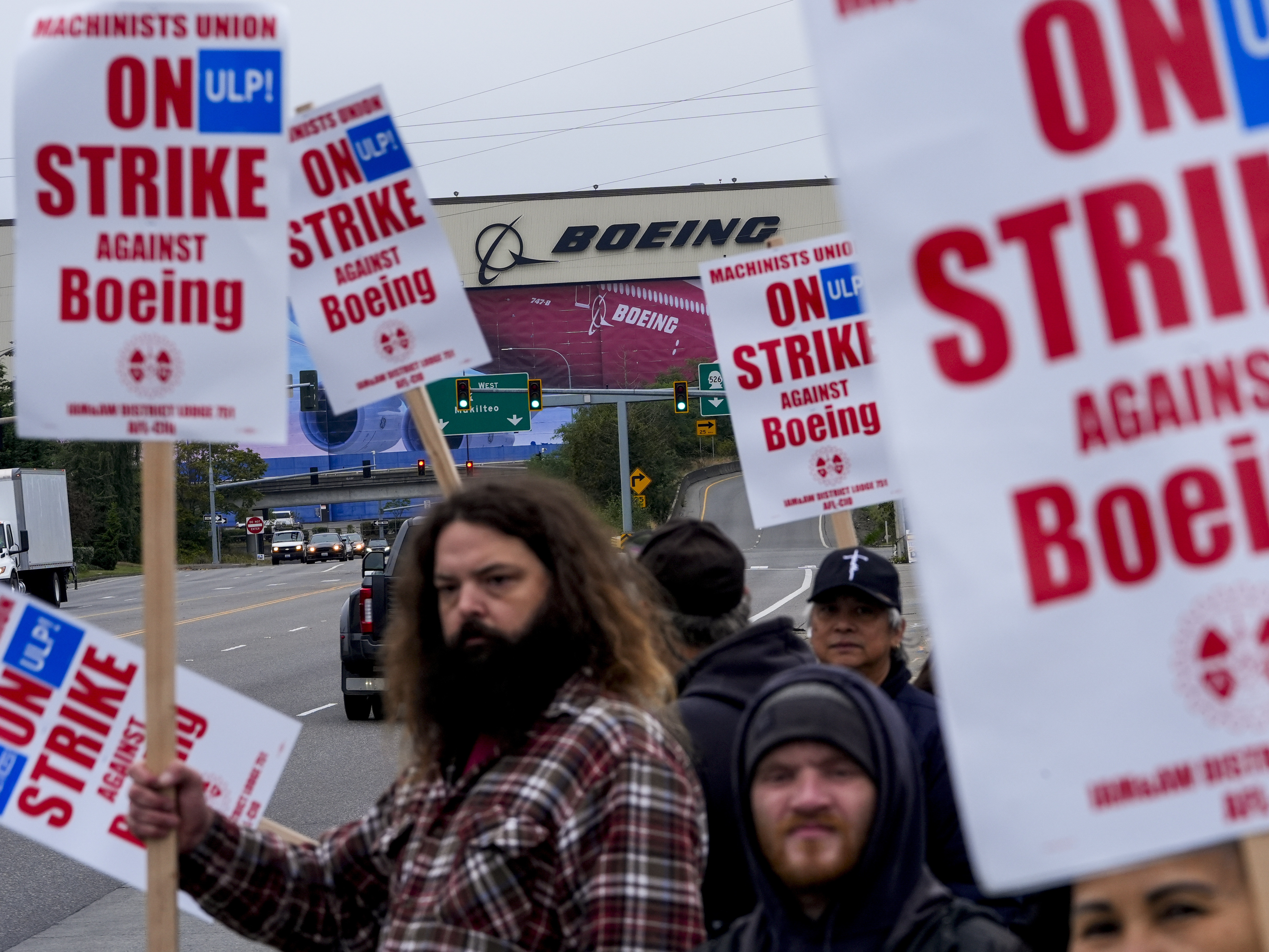 caption: Boeing workers wave picket signs to passing drivers as they strike in Everett, Wash.. The machinists walked off the job more than six weeks ago as they bargain for higher pay and a return of their pension plan.