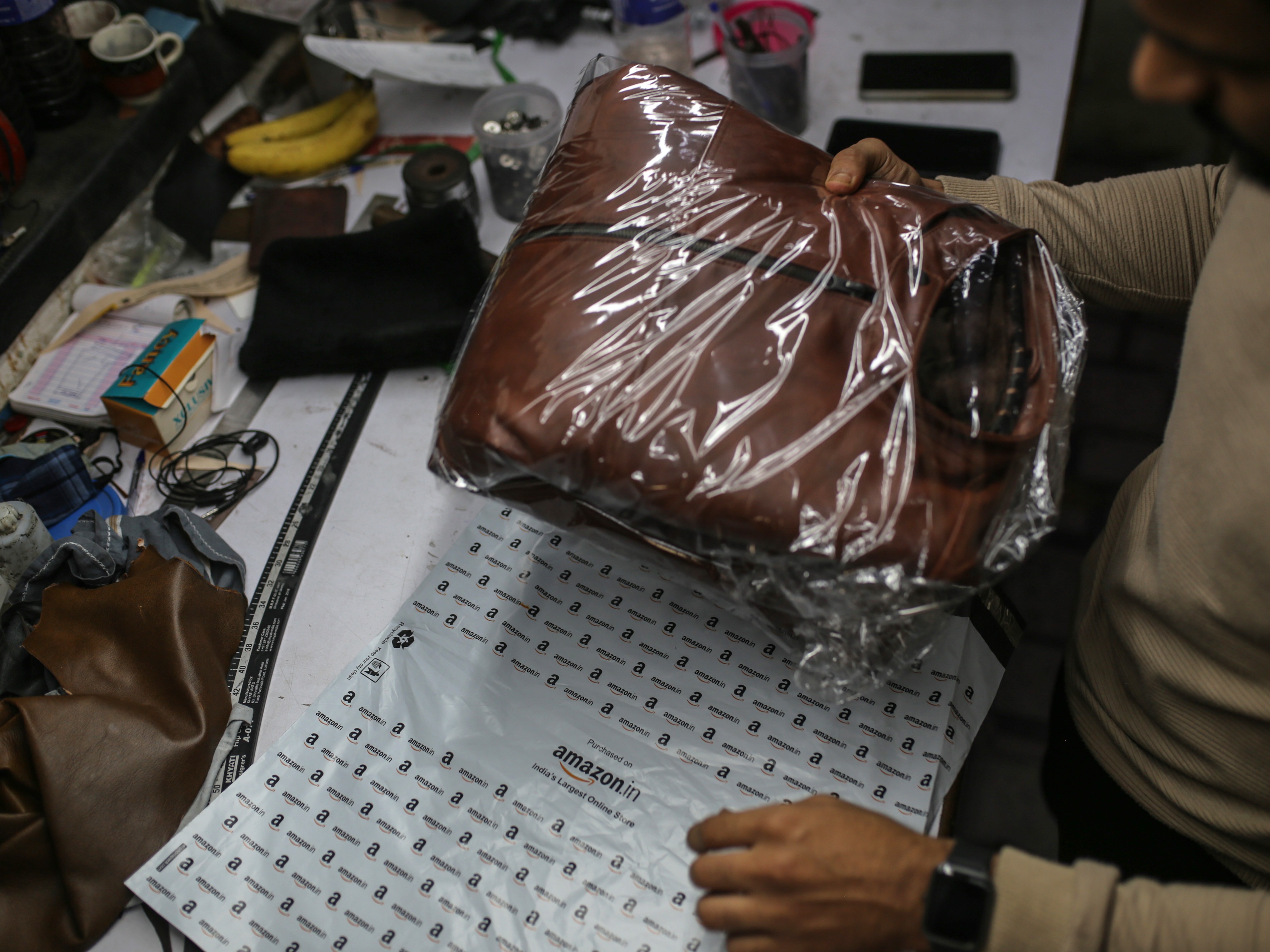 caption: A worker packs a leather jacket in an Amazon India shipping bag at a workshop in the Dharavi area of Mumbai, India, on Jan. 5, 2022.