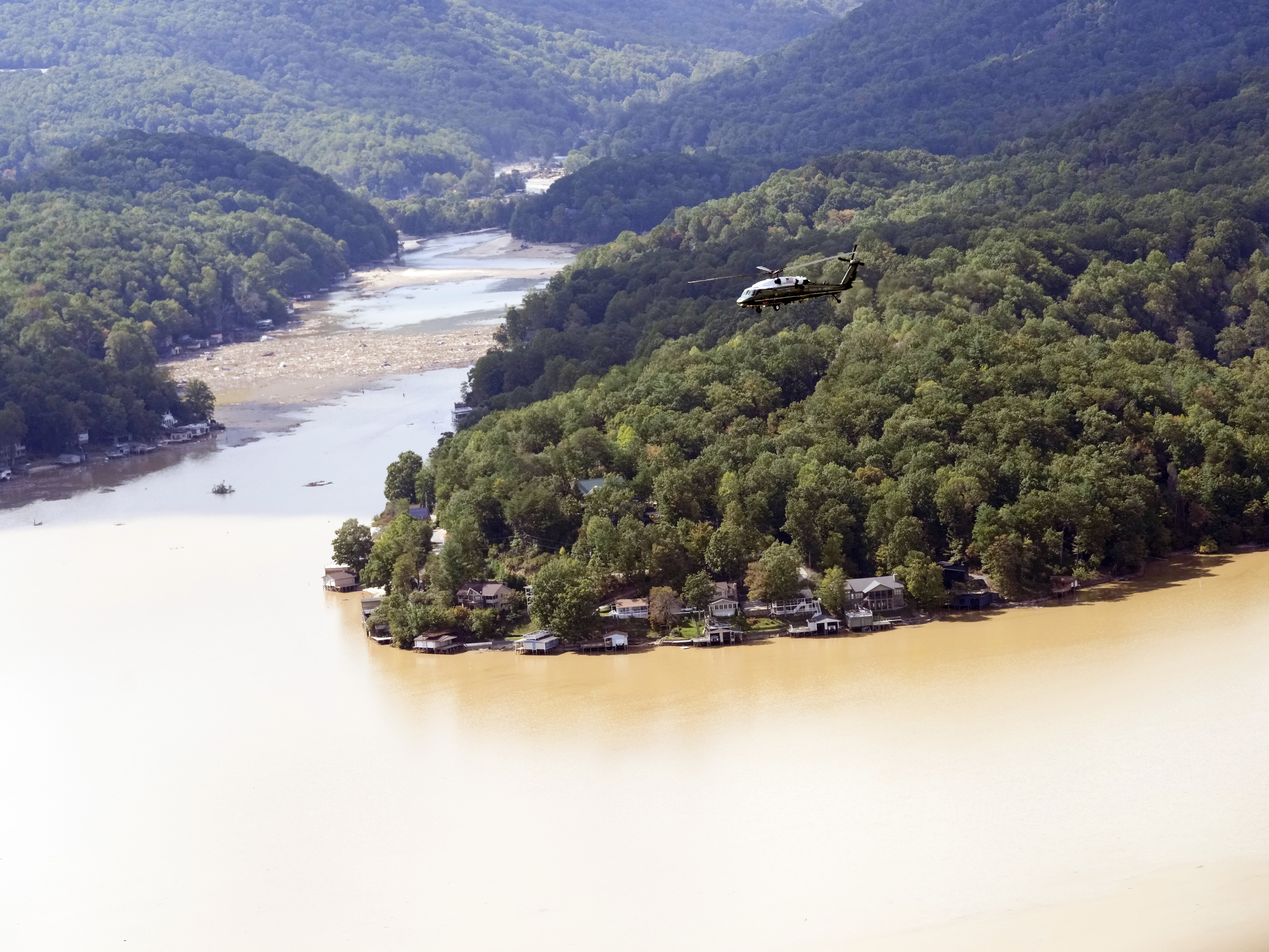 caption: Marine One, with President Biden on board, flies over Lake Lure near Chimney Rock, N.C.,  southwest of the Baxter International plant closed by damage from Hurricane Helene.