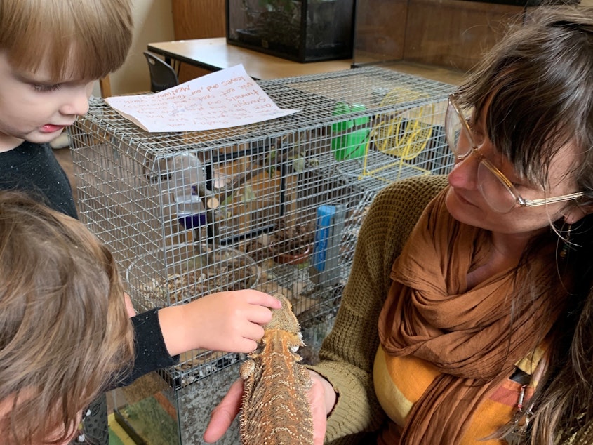 caption: Lainy Morse shows students Wesley Schmidt and Celeste Abraldes a bearded dragon in a photo taken when school was open.