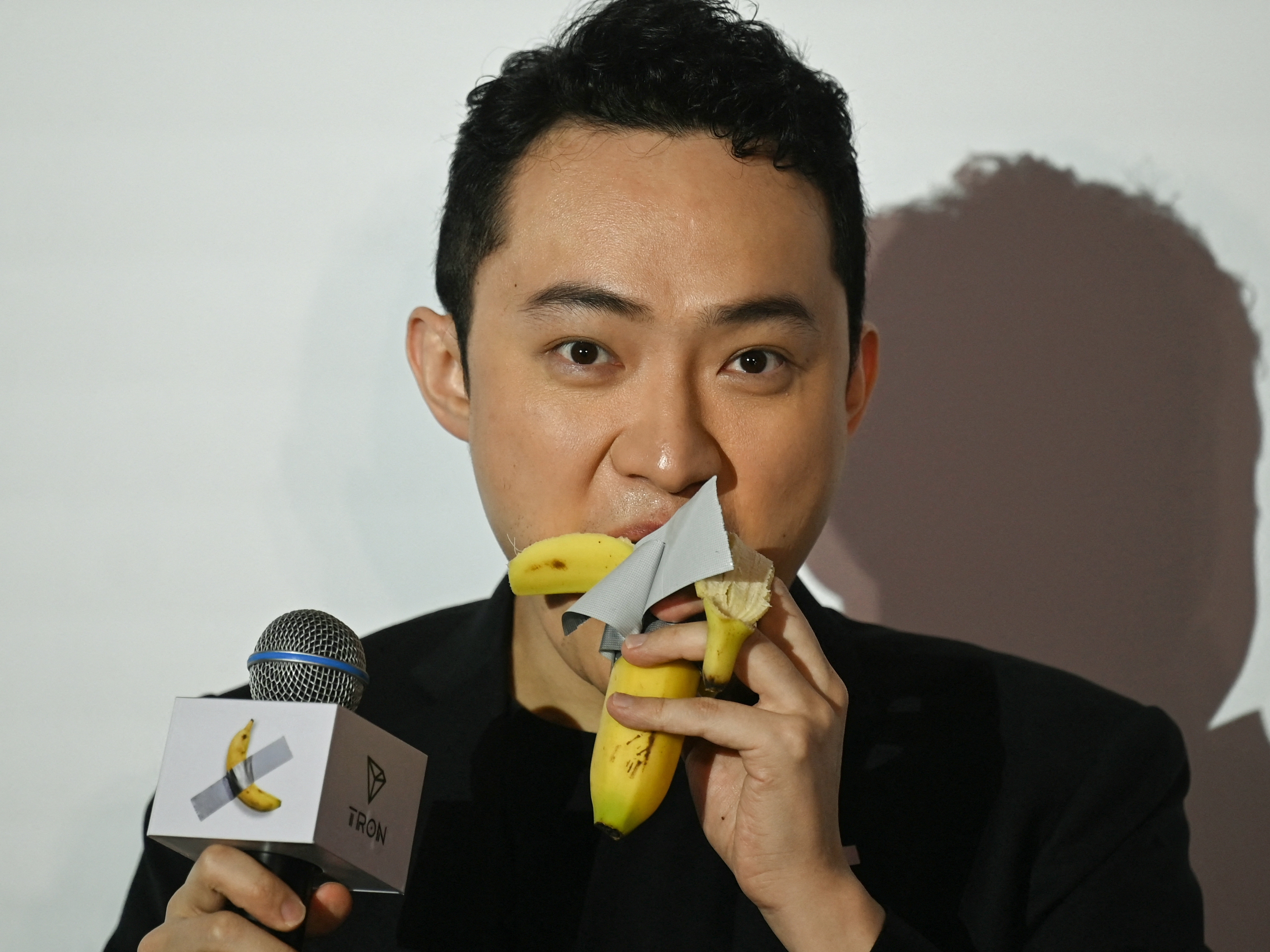 caption: Chinese-born crypto founder Justin Sun eats a banana artwork composed of a fresh banana stuck to a wall with duct tape in Hong Kong on Friday after buying the provocative work of conceptual art by Italian artist Maurizio Cattelan at a New York auction for $6.2 million.