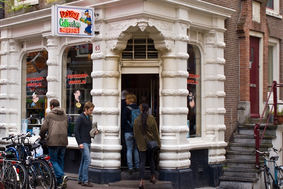 caption: A line extends outside a crowded pot cafe on 'High Street' in Amsterdam.