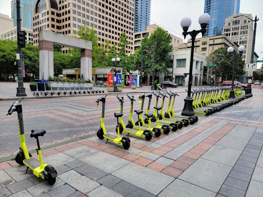 caption: A row of parked LINK scooters face a row parked Bird scooters at Westlake in downtown Seattle on August 10, 2022.