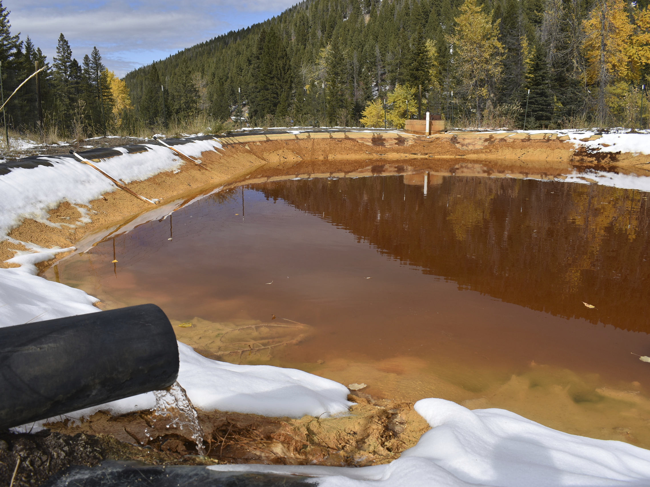caption: At the Upper Tenmile Creek Mining Area Superfund site in 2018, water contaminated with arsenic, lead and zinc flows from a pipe out of the Lee Mountain mine and into a holding pond near Rimini, Mont.
