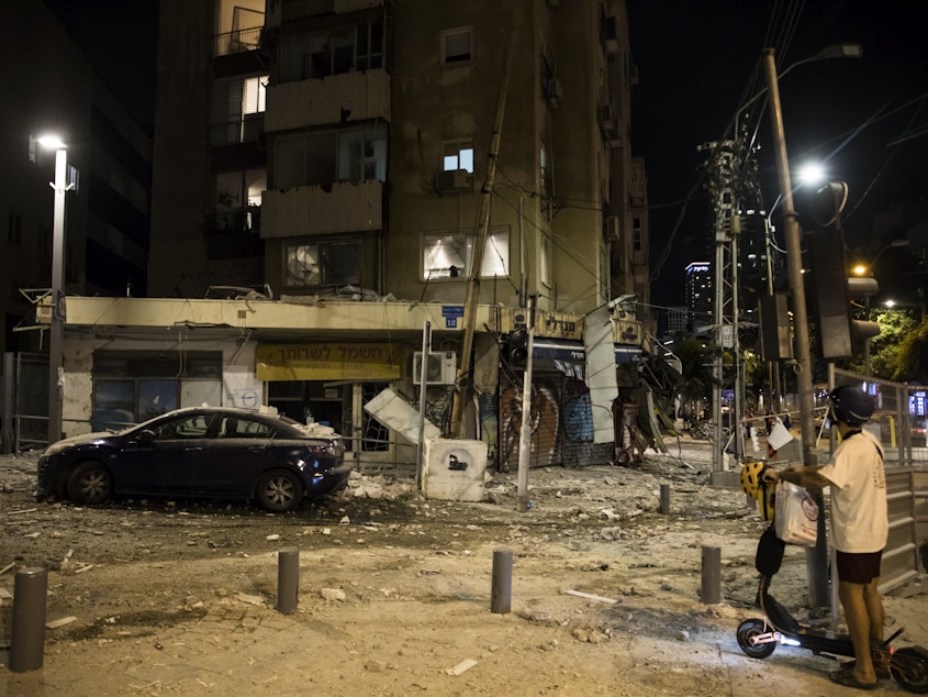 caption: A man passes the scene where a rocket fired from Gaza strip hit a building on Oct. 7, 2023 in Tel Aviv, Israel. Israeli officials revised down the estimated number of people killed in the Oct. 7 attacks to 1,200 from 1,400 on Friday.