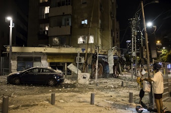 caption: A man passes the scene where a rocket fired from Gaza strip hit a building on Oct. 7, 2023 in Tel Aviv, Israel. Israeli officials revised down the estimated number of people killed in the Oct. 7 attacks to 1,200 from 1,400 on Friday.