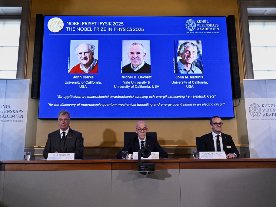 caption: From left, Chair of the Nobel Committee for Physics Chair Olle Eriksson, Secretary General of the Swedish Academy of Sciences Hans Ellegren and Member of the Nobel Committee for Physics Goran Johansson announce Tuesday that John Clarke, Michel H Devoret and John M. Martinis, on screen behind, are the recipients the Nobel Prize in Physics.