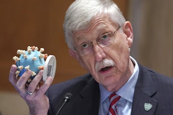 caption: NIH Director Dr. Francis Collins holds up a model of the coronavirus as he testifies before the Senate in May. Collins is retiring as director of the NIH.