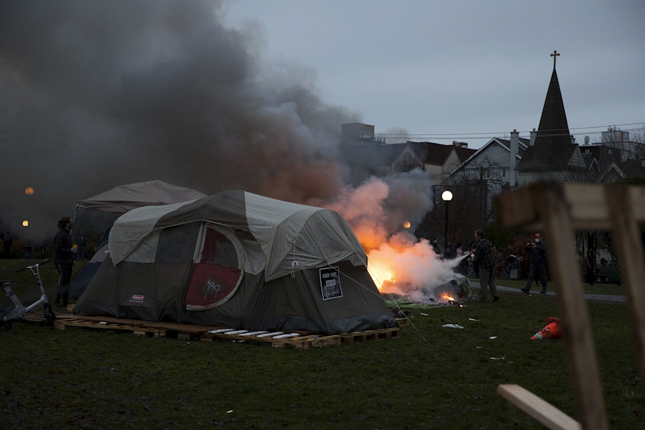 caption: A tent that was set on fire with fireworks is extinguished near the perimeter of an encampment where unhoused community members reside on Wednesday, December 16, 2020, ahead of a scheduled sweep by the Seattle Police Department at Cal Anderson Park in Seattle. 