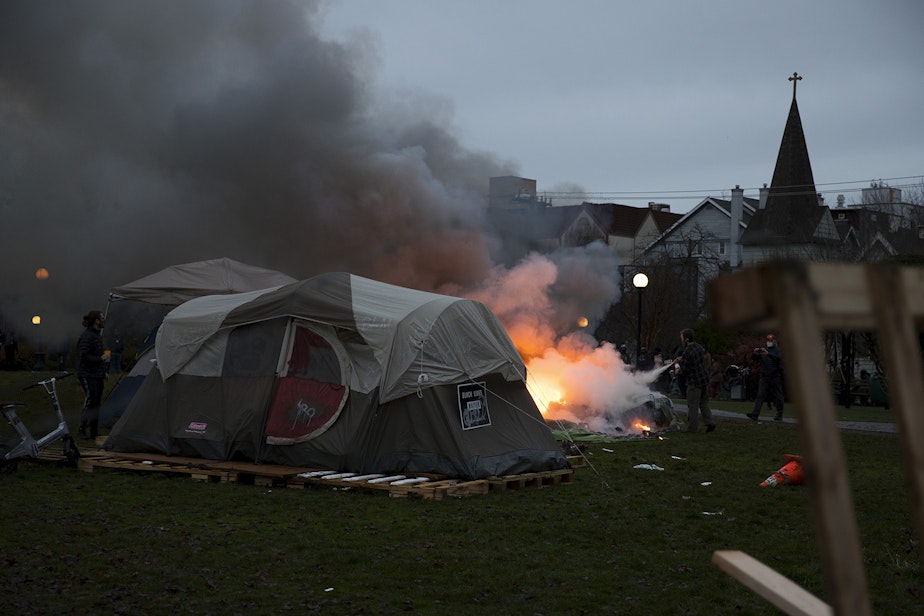 caption: A tent that was set on fire with fireworks is extinguished near the perimeter of an encampment where unhoused community members reside on Wednesday, December 16, 2020, ahead of a scheduled sweep by the Seattle Police Department at Cal Anderson Park in Seattle.
