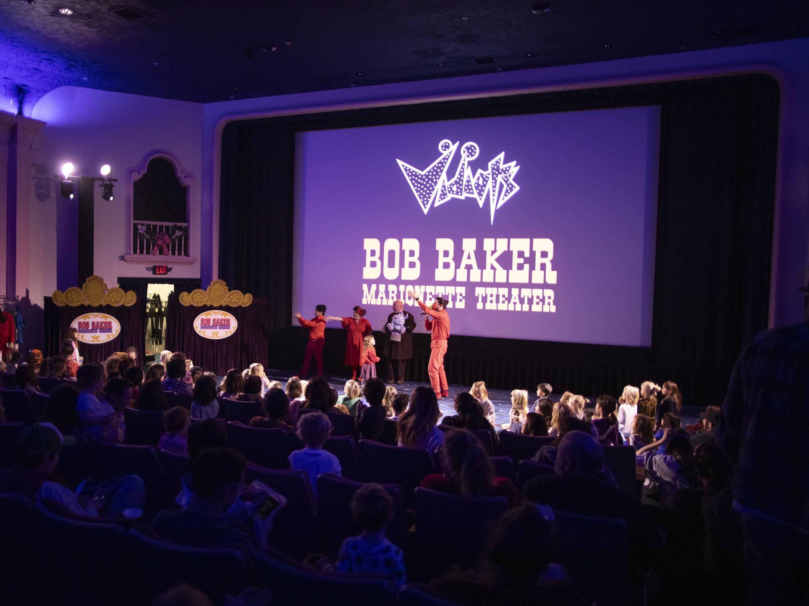 caption: Performers with the Bob Baker Marionette Theater gesture to the crowd of families at Vidiots, a historic theater in northeast Los Angeles, a few miles from where fires are still burning in the Altadena and Pasadena neighborhoods.