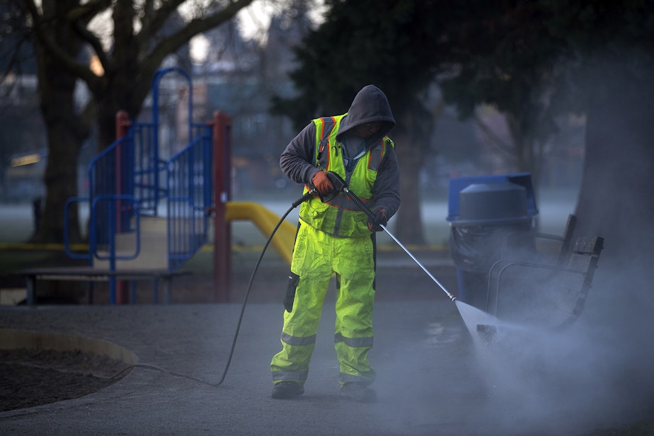caption: File photo: Khai Tran, a utility worker with Seattle Parks and Recreation, sprays water onto a swing-set before a mixture of bleach and water is applied to the West Woodland Park Playground as a result of the coronavirus outbreak on Thursday, March 19, 2020, in Seattle. KUOW Photo/Megan Farmer 
