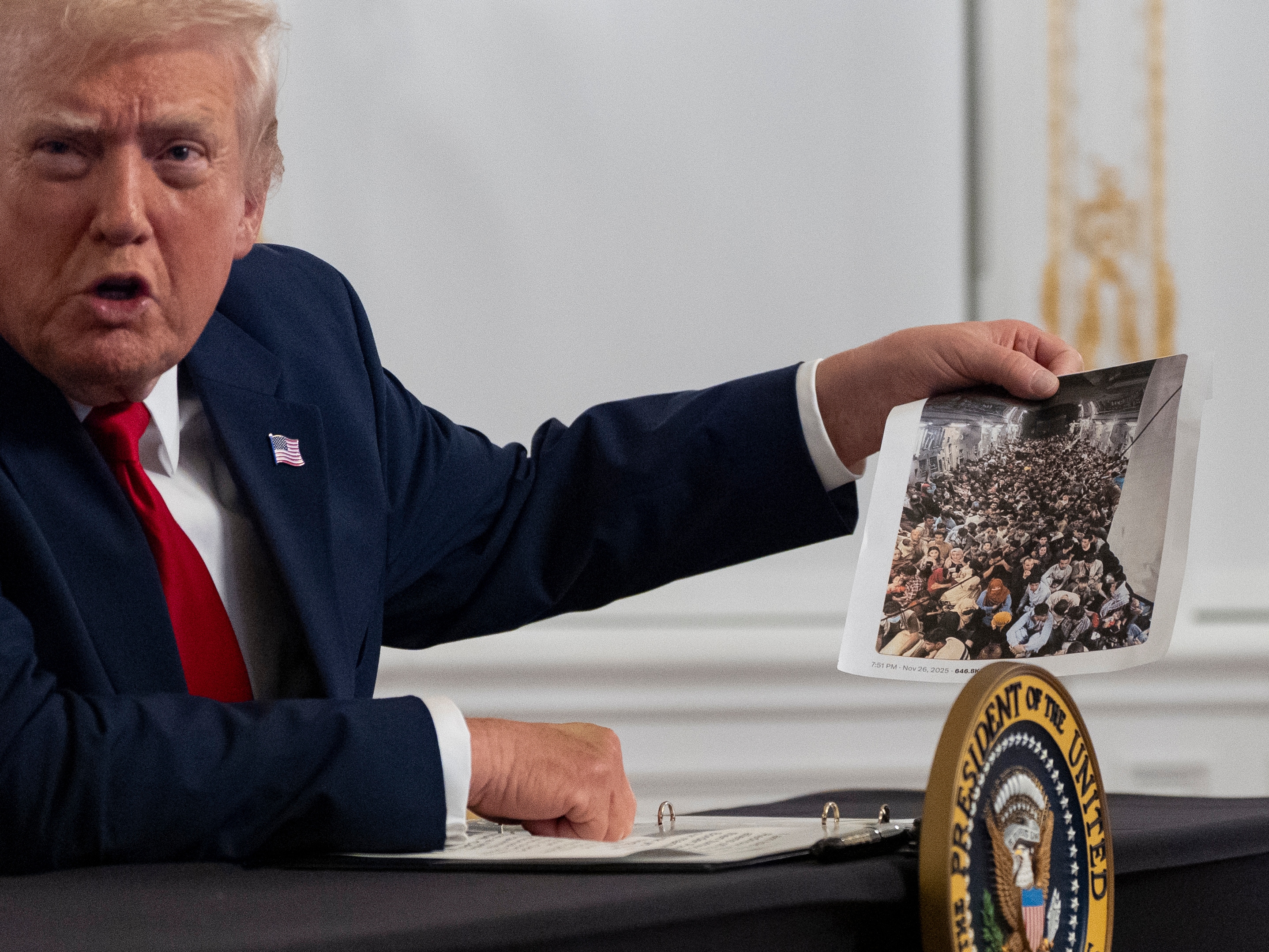 caption: President Donald Trump holds up a photograph as he speaks to reporters after speaking to troops via video from his Mar-a-Lago estate on Thanksgiving, Thursday, Nov. 27, 2025, in Palm Beach, Fla.