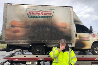 caption: A Lexington, Ky., police officer poses, jokingly, in front of a charred Krispy Kreme truck Monday.