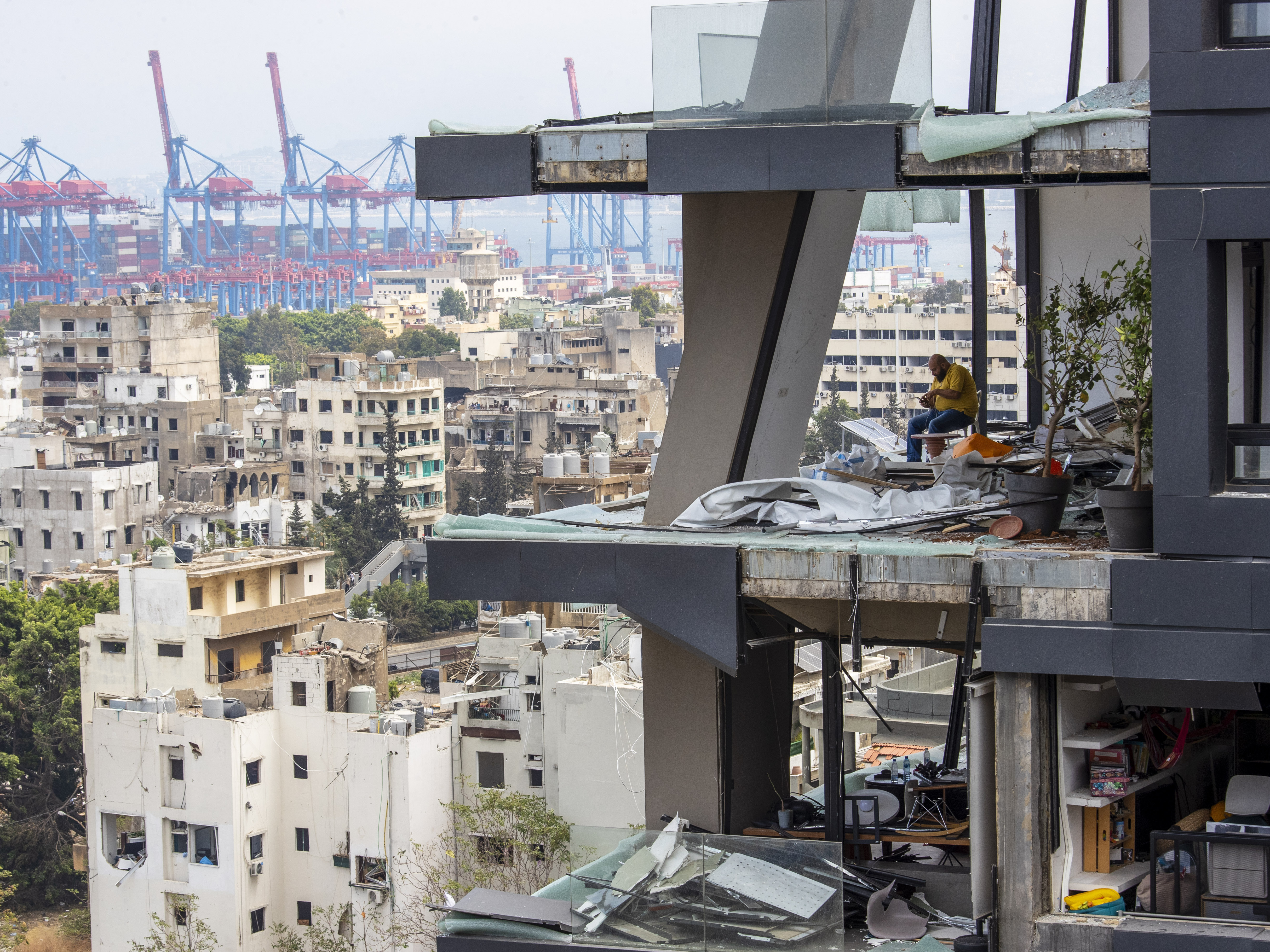 caption: A man sits amid debris inside his home damaged by Tuesday's explosion in Beirut.