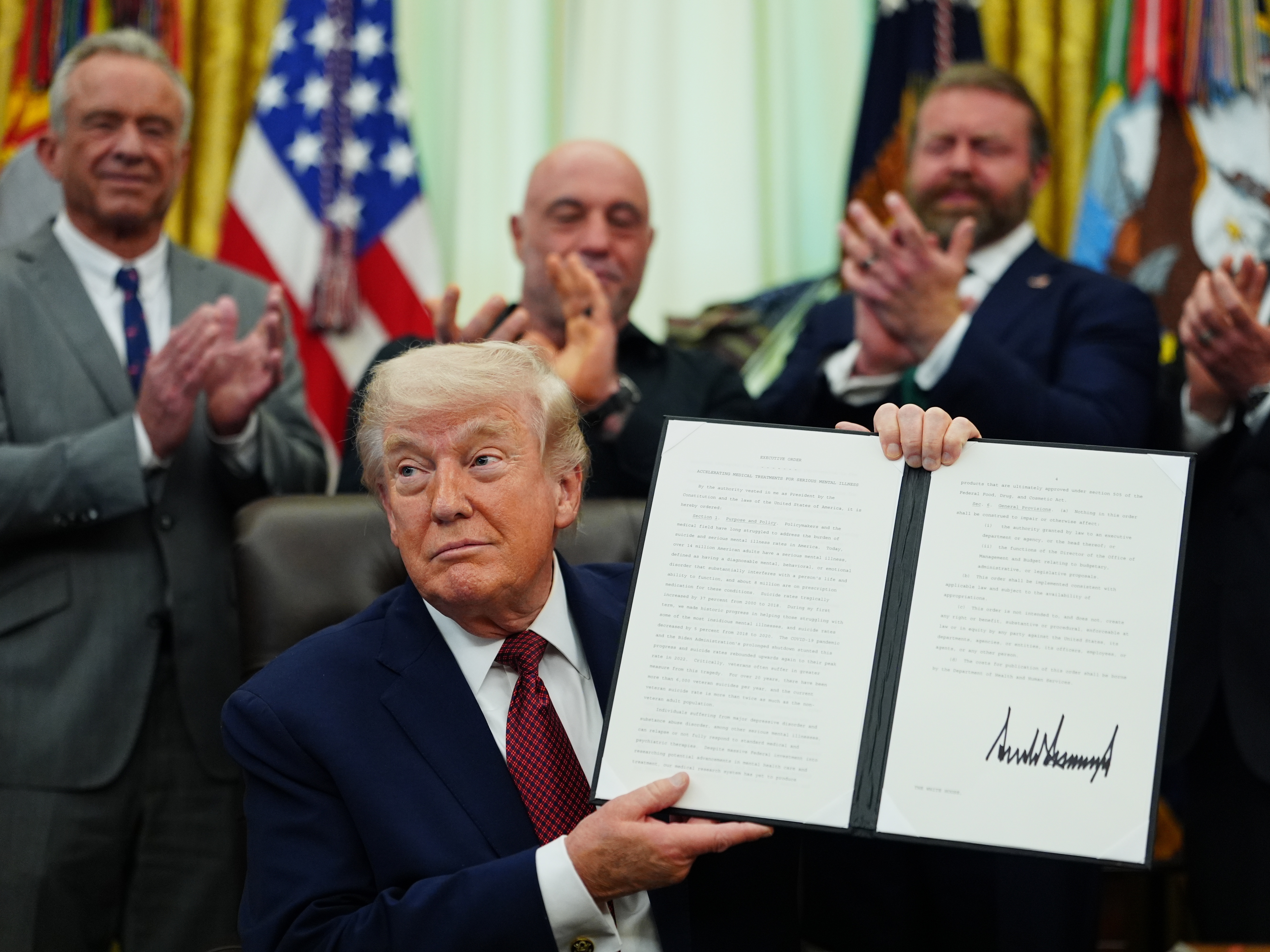 caption: President Donald Trump holds up a signed executive order in the Oval Office of the White House on Saturday in Washington.