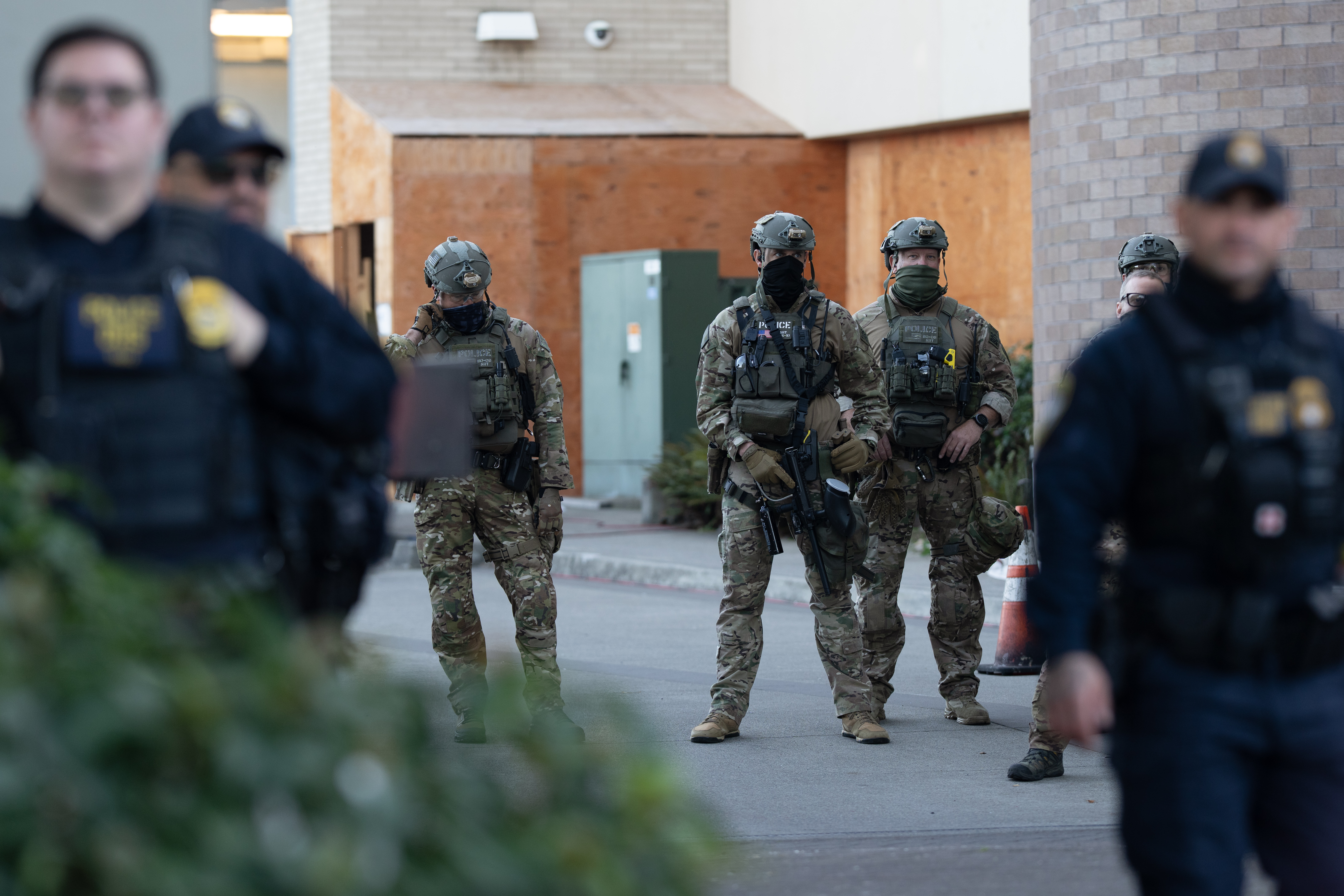 caption: Law enforcement officers watch from a United States Immigration and Customs Enforcement (ICE) facility on Tuesday, Oct. 21, 2025, in Portland, Oregon.
