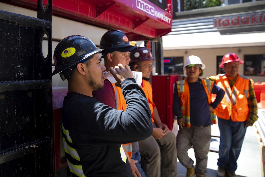 caption: Construction workers including Cristian Ley, left, cool off in the shade during a lunch break at a construction site along Brooklyn Avenue Northeast on Thursday, July 28, 2022, in the University District of Seattle. 