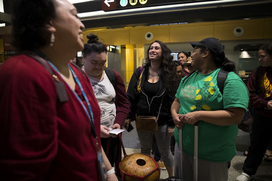 caption: Leilani Kaaiwela-Pedreira, center, laughs with other dancers and musicians as they wait to board a shuttle before flying to Hilo on Friday, March 30, 2018, at Seattle-Tacoma International Airport.