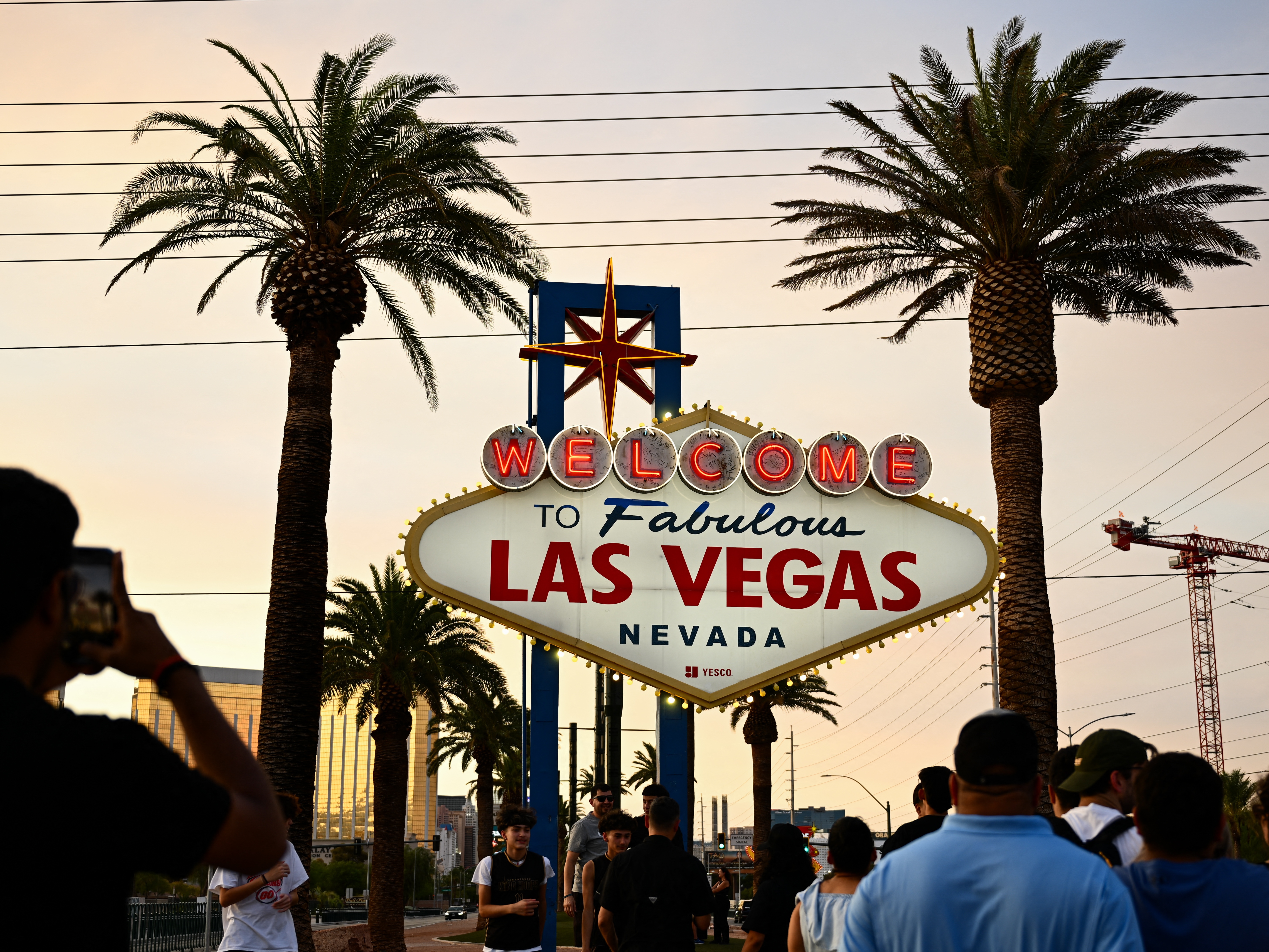 caption: People take pictures with the Welcome To Fabulous Las Vegas sign under hazy orange skies as the sun sets on July 29, 2023.
