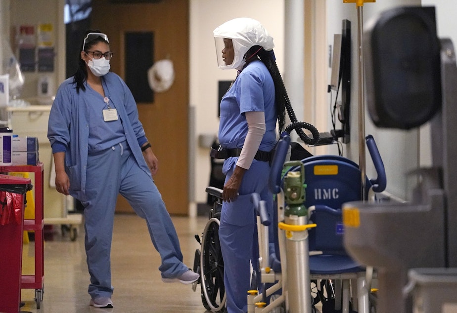 caption: Hospital assistant Tracy Chambers, right, talks with another staff member in a hallway in the acute care unit, where about half the patients are COVID-19 positive or in quarantine after exposure, of Harborview Medical Center, Friday, Jan. 14, 2022, in Seattle. 