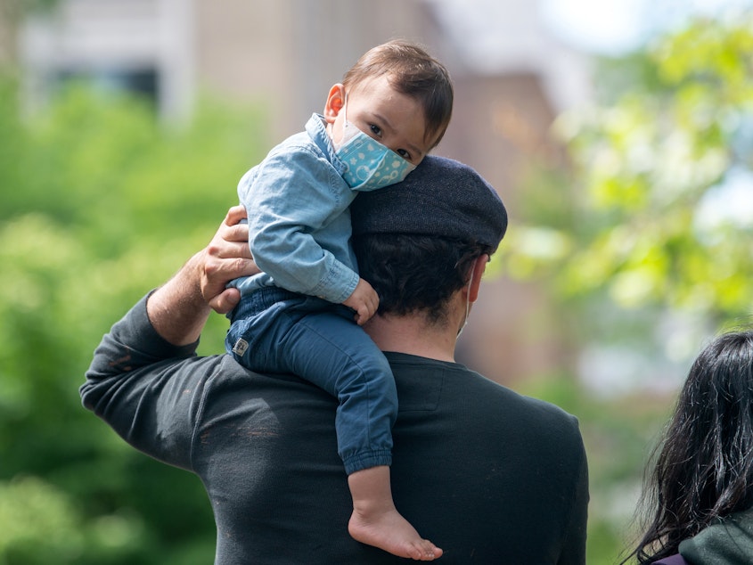 caption: A child wearing a mask sits on his father's shoulder on May 24, 2020 in New York City. Dr. Jose Romero suggested that taking toddlers into the public is a risk.
