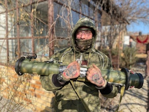 caption: Max, 33, a Ukrainian sniper, poses in the backyard of the reconnaissance team's safe house in the eastern Ukrainian city of Kramatorsk. He's holding a "trophy" — an antitank missile taken off Russian soldiers.