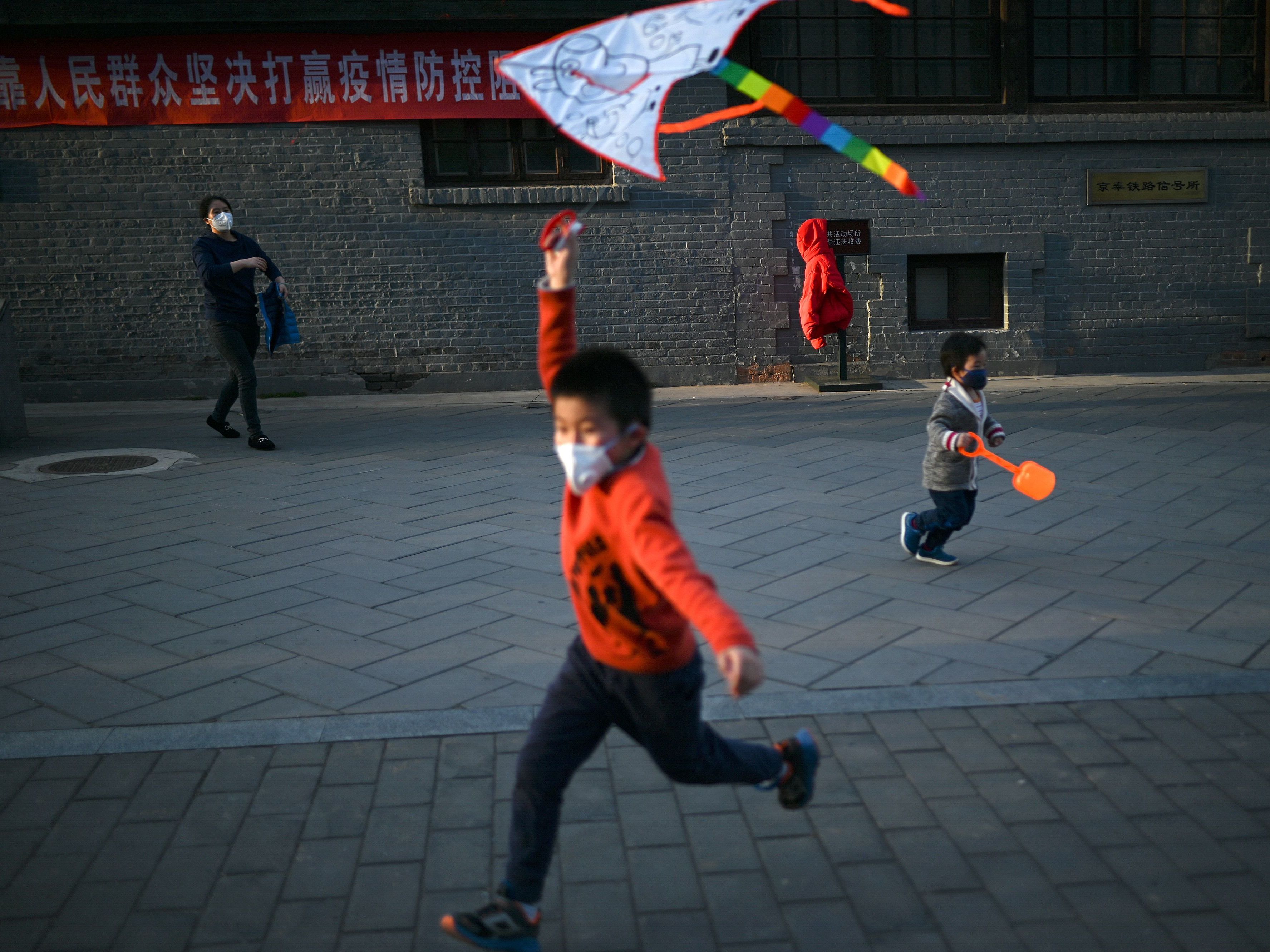caption: A boy wearing a face mask flies a kite at a park in Beijing. Researchers are studying the response of children to COVID-19.
