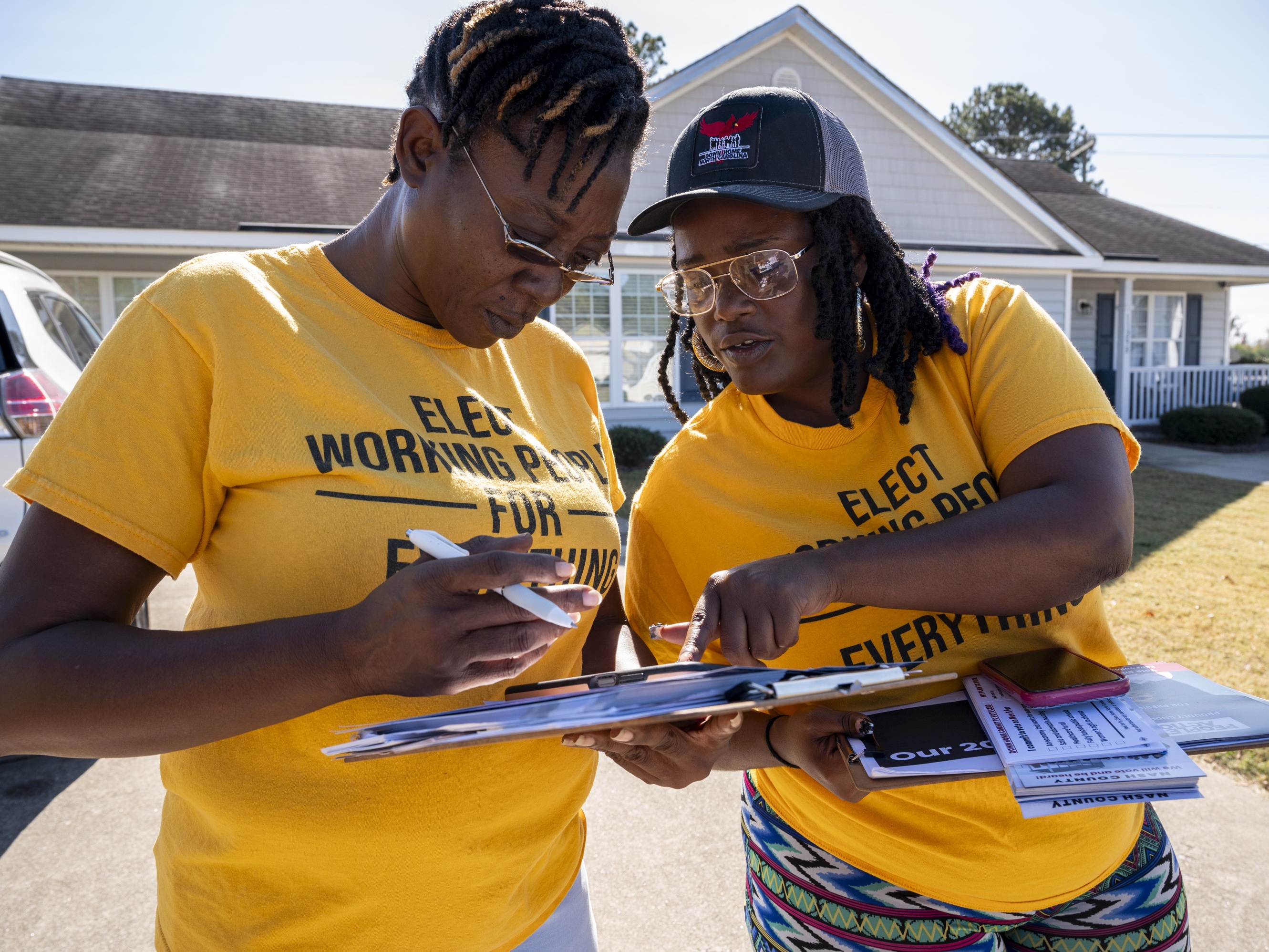 caption: Andrea Farmer (left) and Alex Cook mark off homes they have visited on their app while canvassing in a neighborhood in Nashville, North Carolina in October.