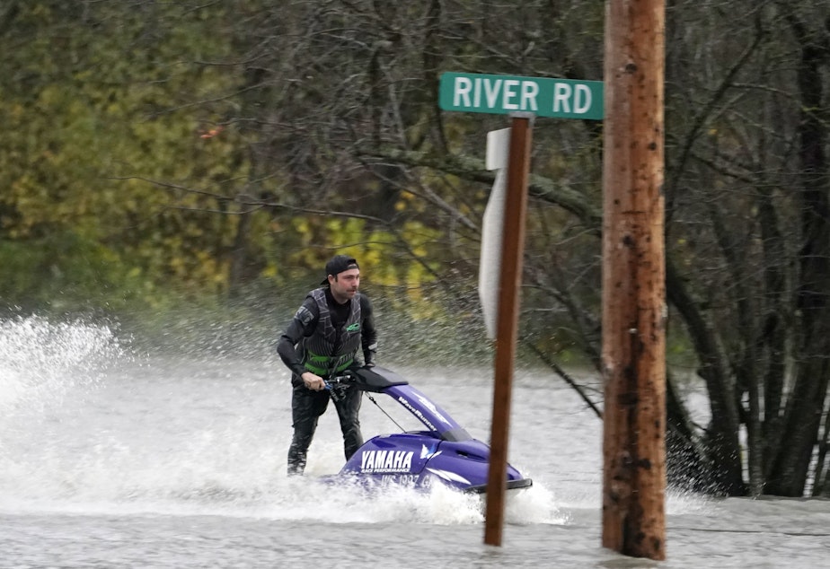 caption: A man operates a personal watercraft along a road flooded by water from the Skagit River, on Monday in Sedro-Woolley, Wash.