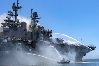 caption: Police boats combat a fire aboard the amphibious assault ship USS Bonhomme Richard at Naval Base San Diego on Sunday.