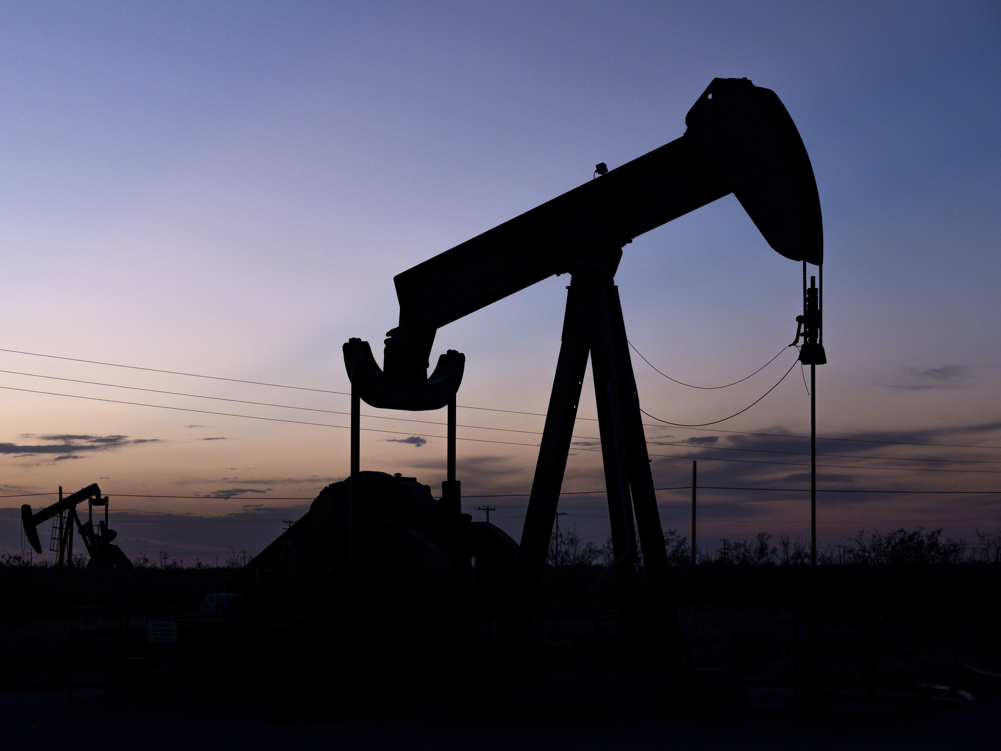 caption: The sun sets behind pumpjacks on Sept. 15, 2021, in the oilfields of Penwell, Texas.
