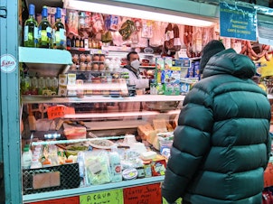 caption: A vendor wearing protective masks and gloves serves a customer at a market in Rome on April 16.