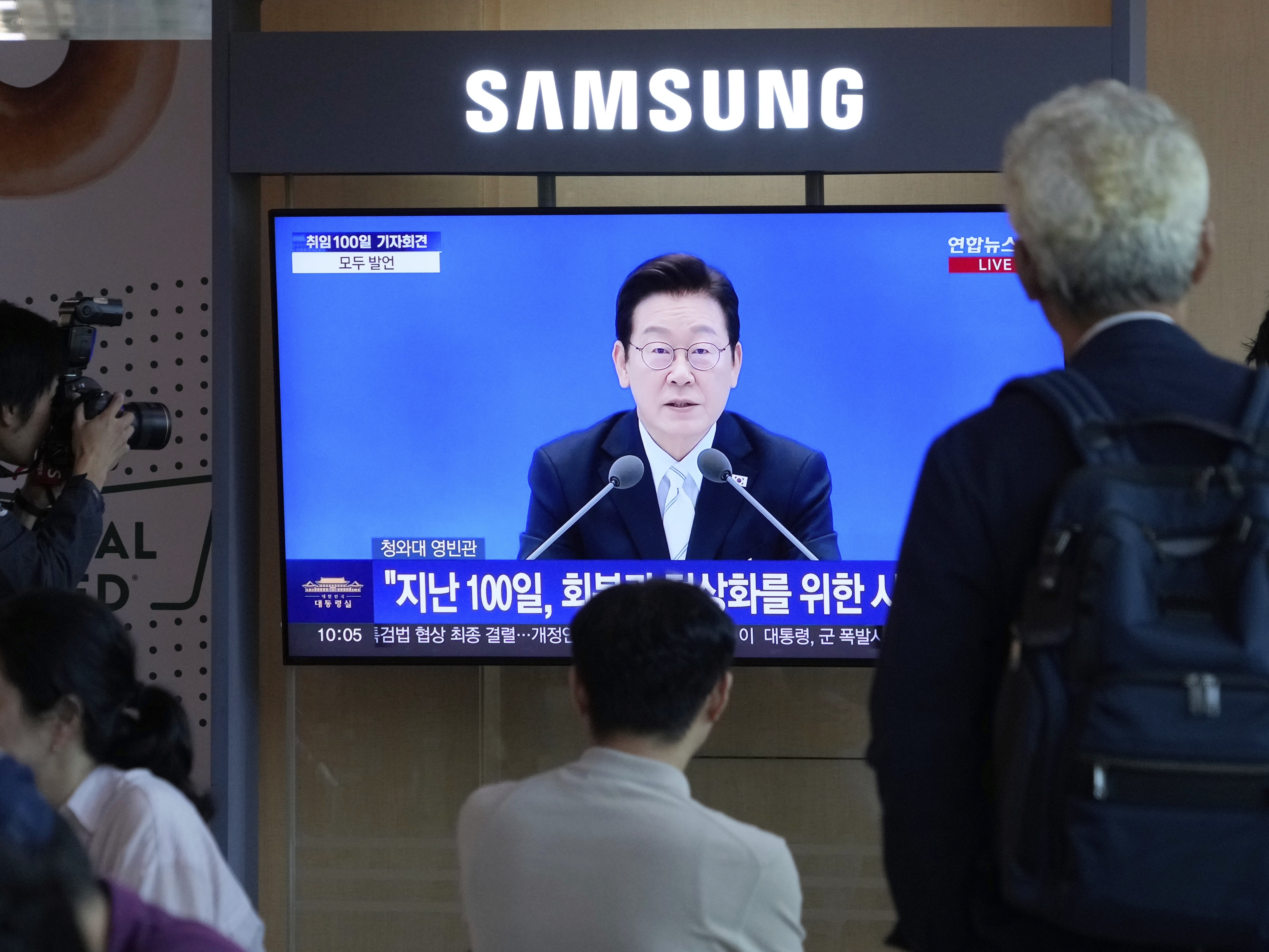 caption: People watch a TV screen showing the live broadcast of South Korean President Lee Jae Myung's press conference at the Seoul Railway Station in Seoul, South Korea, Thursday.