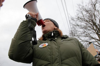 caption: Leslie Brown, an activist with Edmonds Neighborhood Action Coalition, shouted into a bullhorn to rally dozens of protesters gathered outside the Edmonds PCC.
