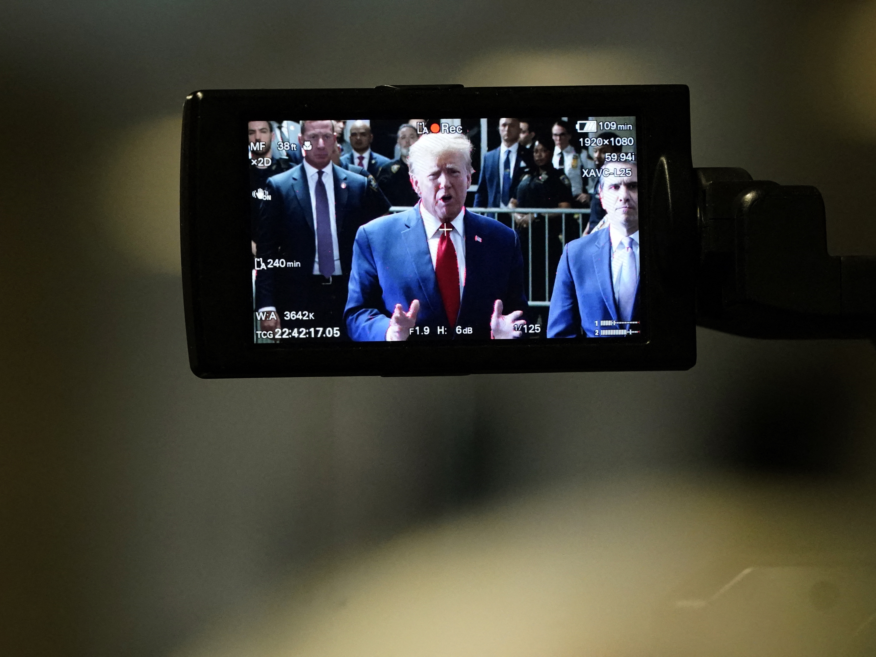 caption: Former President Donald Trump, on a camera monitor, speaks to the press as he arrives at Manhattan Criminal Court on Feb. 15 for a hearing in his case of paying hush money to cover up extramarital affairs.