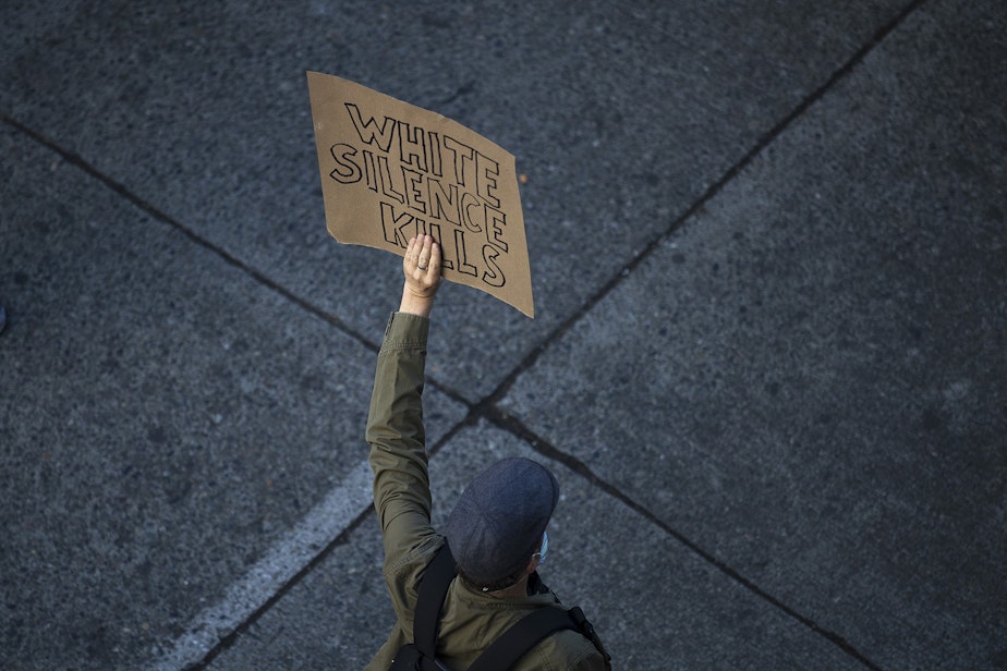 caption: FILE: An individual demonstrating for racial justice holds a sign that reads 'White Silence Kills,' on Sunday June 7, 2020, near Cal Anderson Park in Seattle.