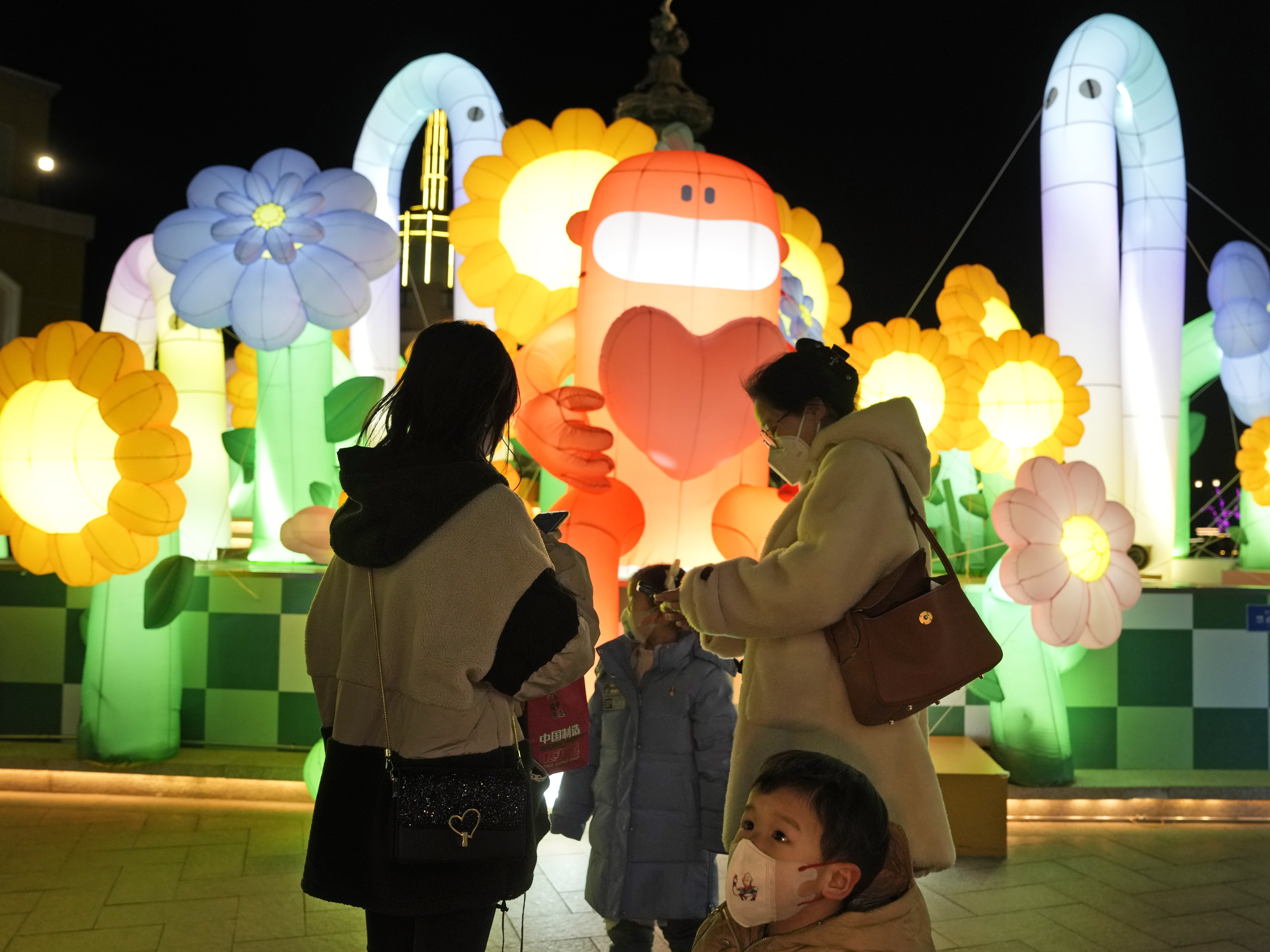 caption: A child wearing a mask stands near light decorations at a mall in Beijing on Friday. China is on a bumpy road back to normal life as schools, shopping malls and restaurants fill up again following the abrupt end of some of the world's most severe restrictions even as hospitals are swamped with COVID-19 patients.