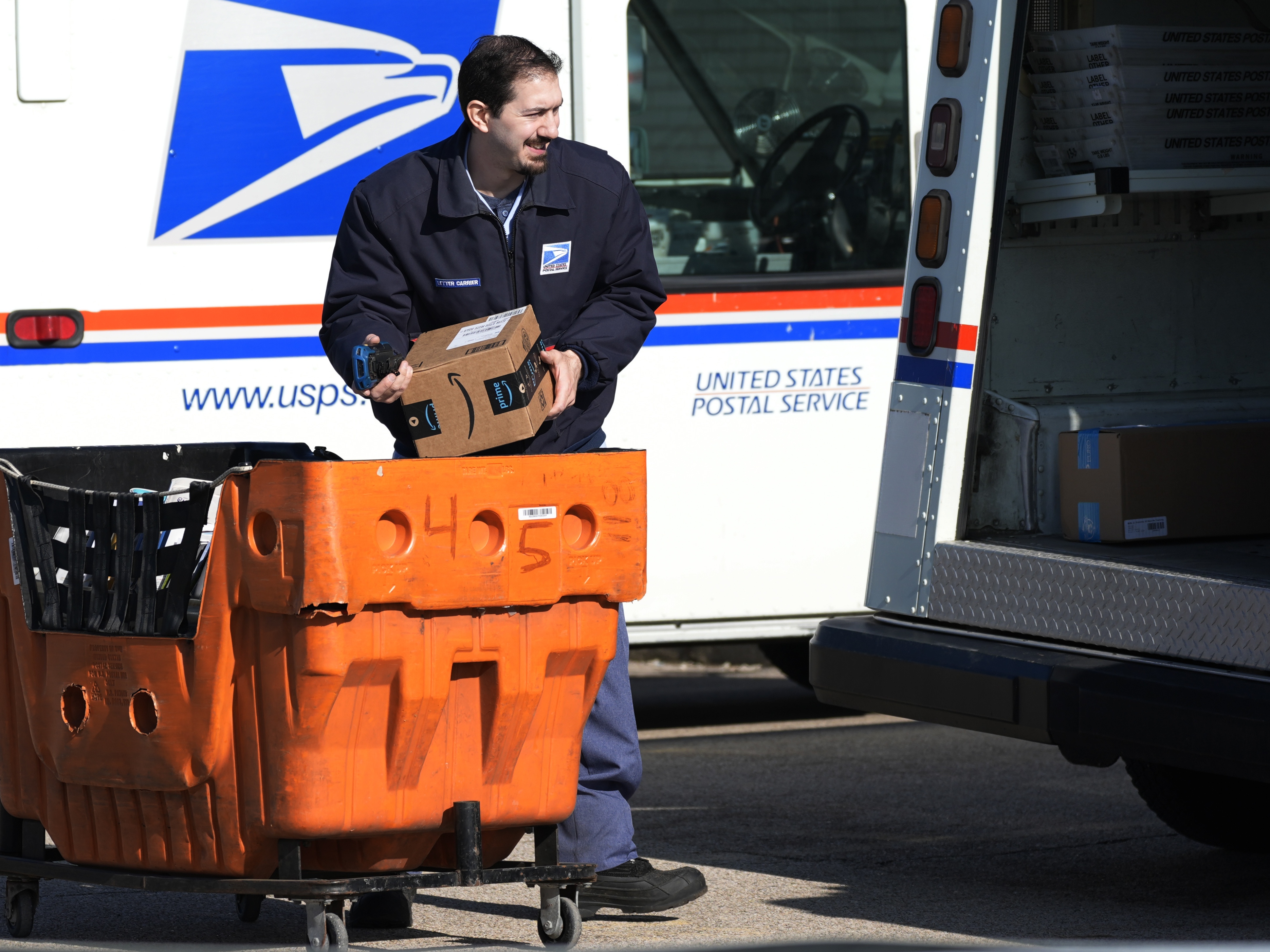 caption: A U.S. Postal Service employee is shown loading parcels outside a post office in Wheeling, Ill., on Jan. 29, 2024.