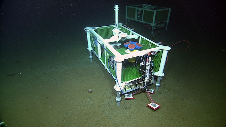 caption: An Acousitic Doppler Current Profiler (four blue-red cyllinders with yellow housing) is installed at the base of Axial Seamount. 